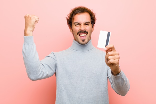 Young handsome man with a credit card  pink flat wall