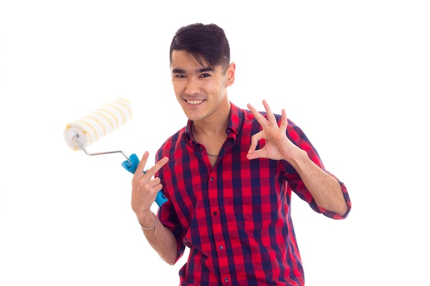 Young handsome man with dark hair in red plaid shirt holding white roll and showing OKAY