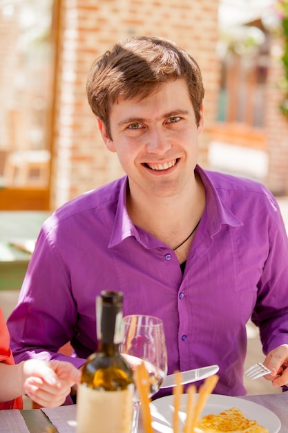 Young handsome man with glass of wine and dishes in restaurant in summertime.