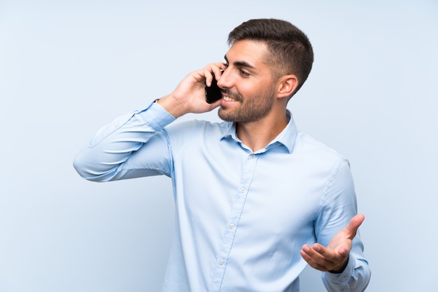 Giovane uomo bello con il suo cellulare sopra la parete blu isolata