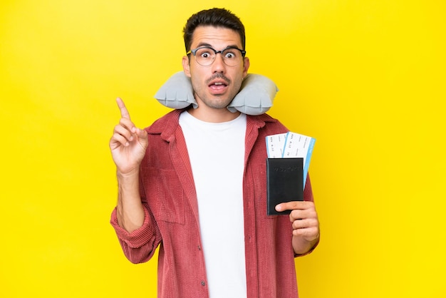 Young handsome man with Inflatable Travel Pillow over isolated yellow background thinking an idea pointing the finger up