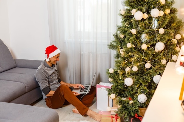 Young handsome man with laptop in Christmas setting at home.