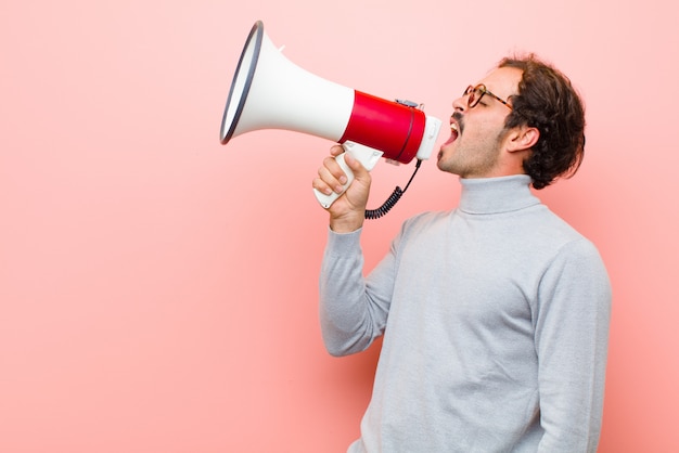 Young handsome man with a megaphone against pink flat wall