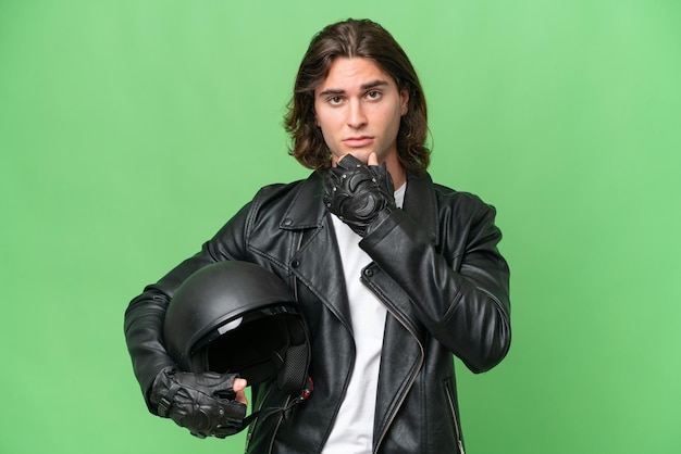 Young handsome man with a motorcycle helmet isolated on green chroma background thinking