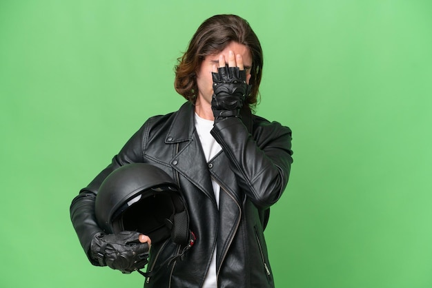 疲れや病気の表情で緑の彩度の背景に分離されたオートバイのヘルメットを持つ若いハンサムな男