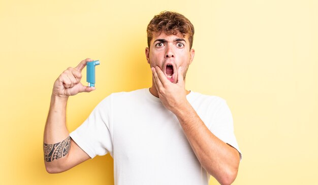 young handsome man with mouth and eyes wide open and hand on chin. asthma concept