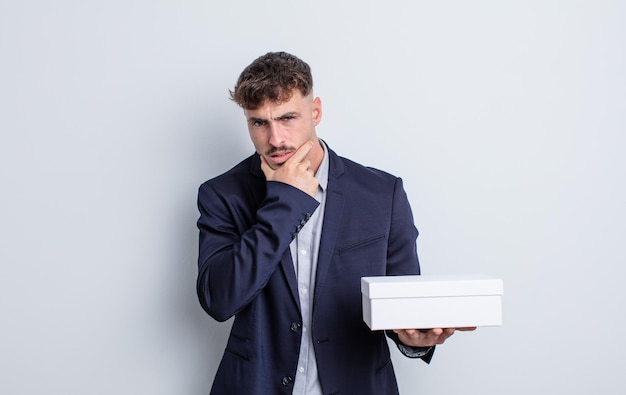 Young handsome man with mouth and eyes wide open and hand on chin. white box package