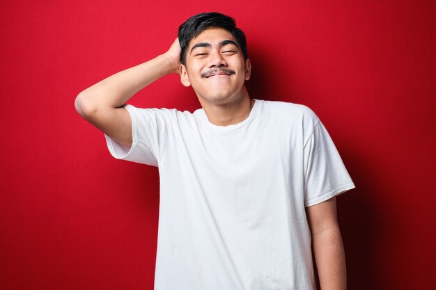 Photo young handsome man with mustache wearing white t-shirt standing over red background confuse and wonder about question. uncertain with doubt, thinking with hand on head. pensive concept.