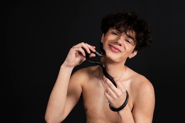 Young handsome man with naked torso with a black snake crawling on his arms or hands Isolated on black background