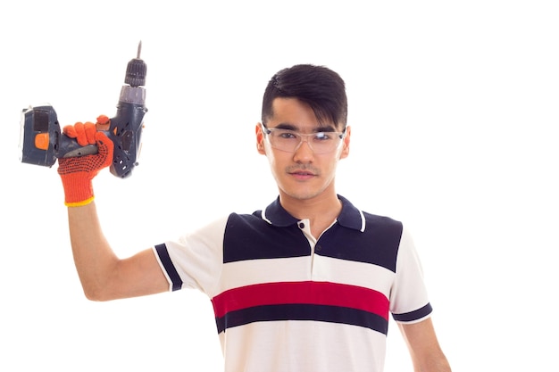 Young handsome man with orange gloves and protective glasses holding grey electric screwdriver