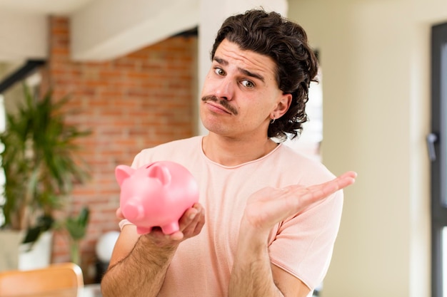 Young handsome man with a piggy bank savings concept at home interior