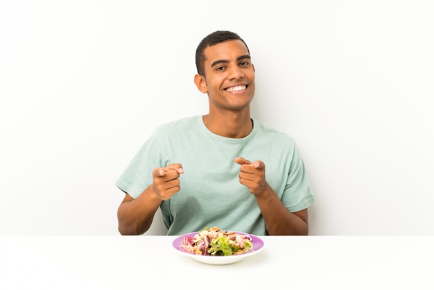 Young handsome man with salad in a table points finger at you