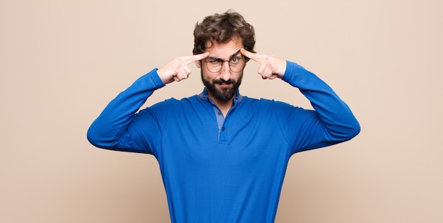 Giovane uomo bello con uno sguardo serio e concentrato, che fa brainstorming e pensa a un problema impegnativo contro la parete piatta