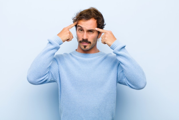 Young handsome man with a serious and concentrated look, brainstorming and thinking about a challenging problem isolated over flat wall