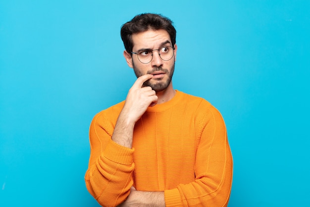 Young handsome man with surprised, nervous, worried or frightened look, looking to the side towards copy space