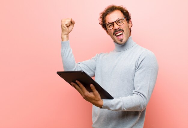 Young handsome man with a tablet  pink flat wall