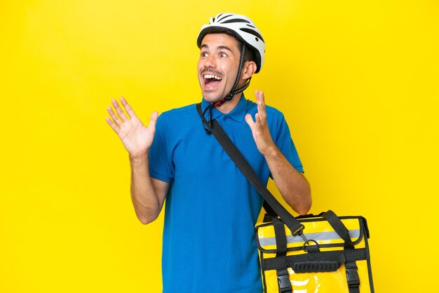 Young handsome man with thermal backpack over isolated yellow background with surprise facial expression