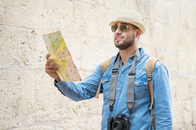 Foto giovane bell'uomo con una mappa turistica che si guarda intorno per la strada della città