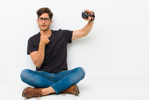 Young handsome man with a vintage camera sitting on the floor sitting on the floor in a white room