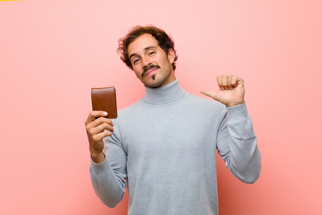 Young handsome man with a wallet against pink flat wall