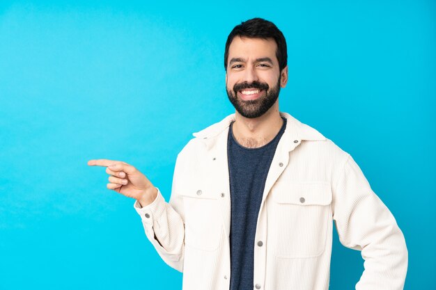 Young handsome man with white corduroy jacket over isolated blue wall pointing finger to the side