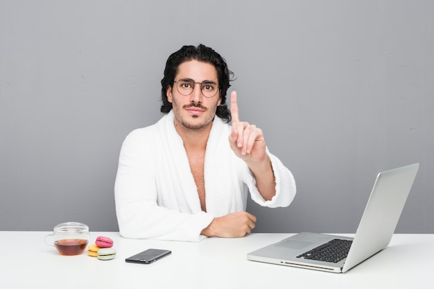 Young handsome man working after a shower showing number one with finger