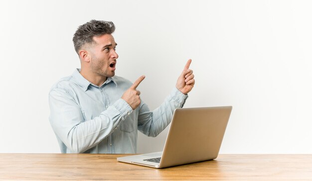 Young handsome man working with his laptop pointing with forefingersa , expressing excitement and desire.