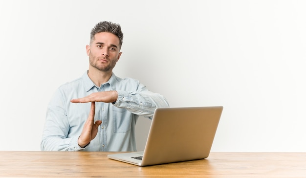 Giovane uomo bello che lavora con il suo computer portatile che mostra un gesto di timeout.