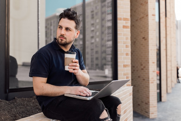 Young handsome man working with laptop and smartphone online on the street