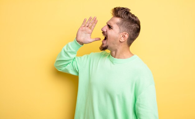 Young handsome man yelling loudly and angrily to copy space on the side with hand next to mouth strange moustache concept