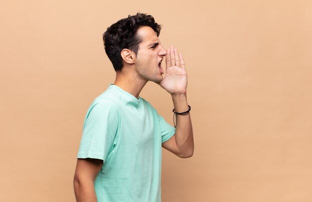 Photo young handsome man yelling loudly and angrily to copy space on the side, with hand next to mouth