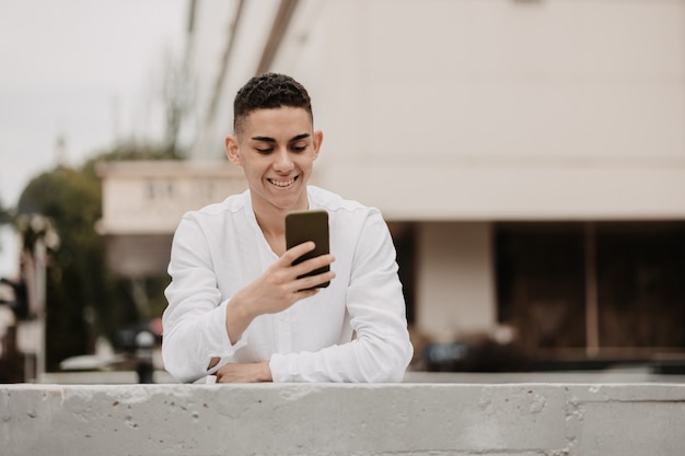 Young handsome model with a cellphone. Man smiling outside.