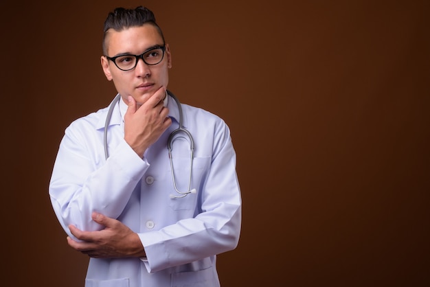 Young handsome multi-ethnic man doctor on brown