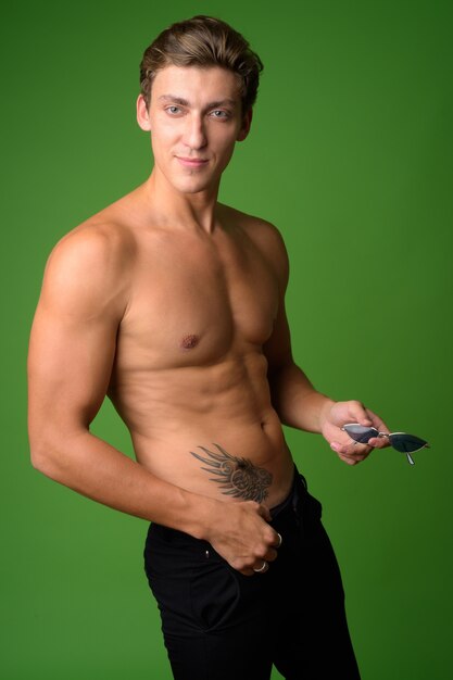 Young handsome muscular man shirtless against green wall