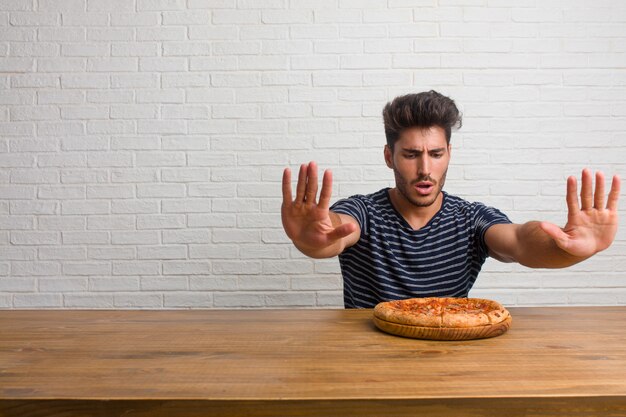 Young handsome and natural man sitting on a table serious and determined, putting hand in front