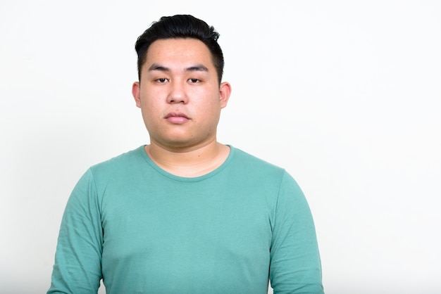 young handsome overweight Filipino man against white wall