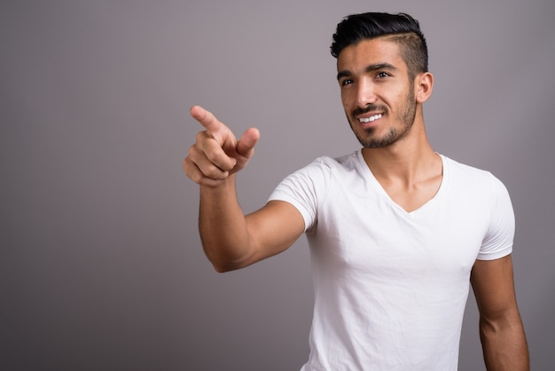 Young handsome Persian man against gray background