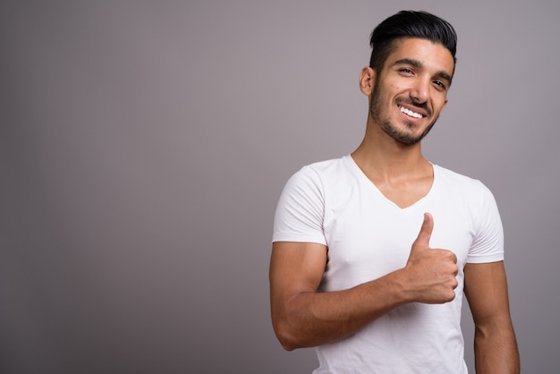 Young handsome Persian man against gray background