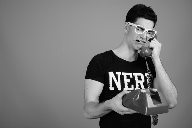 young handsome Persian nerd man with eyeglasses against gray wall in black and white