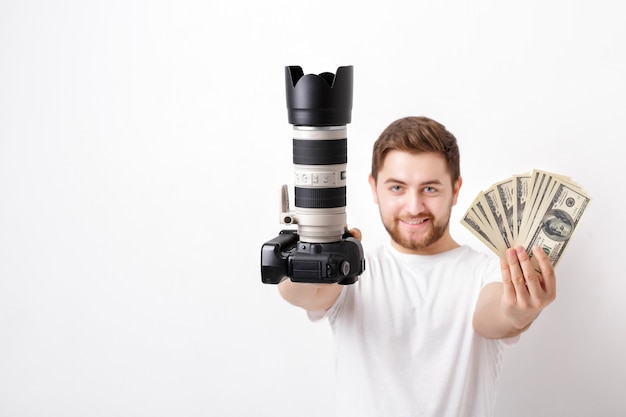 Young handsome photographer with a beard in a white shirt holding a camera and hundred dollar bills. payment for the photo shoot