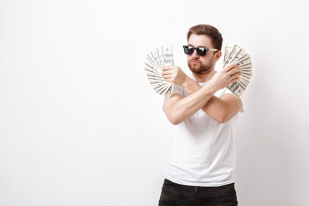 Foto giovane uomo serio bello con la barba in una camicia bianca che tiene un sacco di banconote da cento dollari. soldi