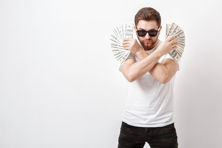 Photo young handsome serious man with a beard in a white shirt holding a lot of hundred-dollar bills. money