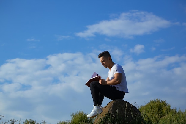 Молодой красивый серьезный мужчина с мускулистым сексуальным телом и голой грудью сидит с ноутбуком на открытом воздухе в солнечный день на фоне голубого неба