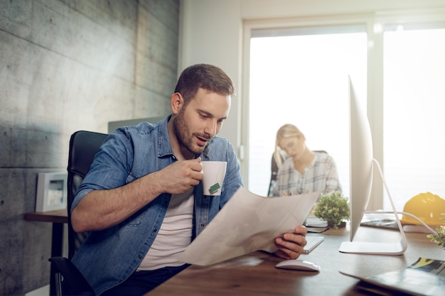 Giovane freelance serio e pensieroso che lavora su un nuovo progetto in ufficio. stanno guardando il progetto e bevono il tè.