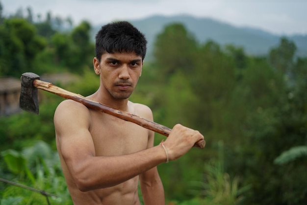 Young handsome shirtless boy holding axe in his shoulders