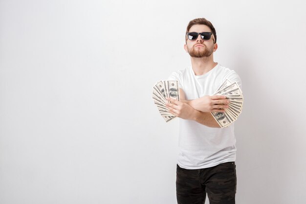 Photo young handsome smiling man with a beard in a white shirt holding a lot of hundred-dollar bills. money