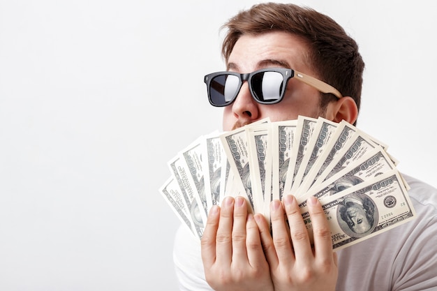 Young handsome smiling man with a beard in a white shirt holding a lot of hundred-dollar bills. money