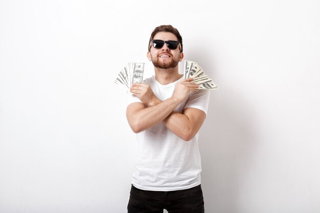 Photo young handsome smiling man with a beard in a white shirt and sunglasses holding a lot of hundred-dollar bills. money