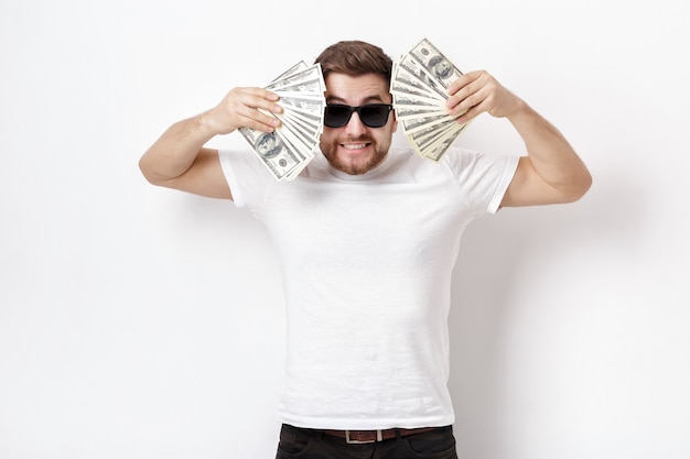 Young handsome smiling man with a beard in a white shirt and sunglasses holding a lot of hundred-dollar bills. money