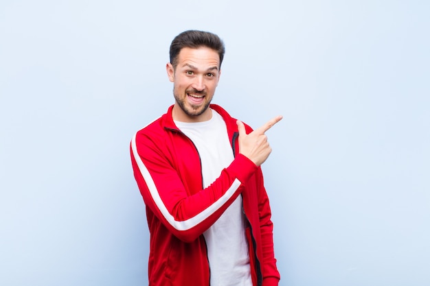 Young handsome sports man or monitor looking excited and surprised pointing to the side and upwards to copy space against green wall